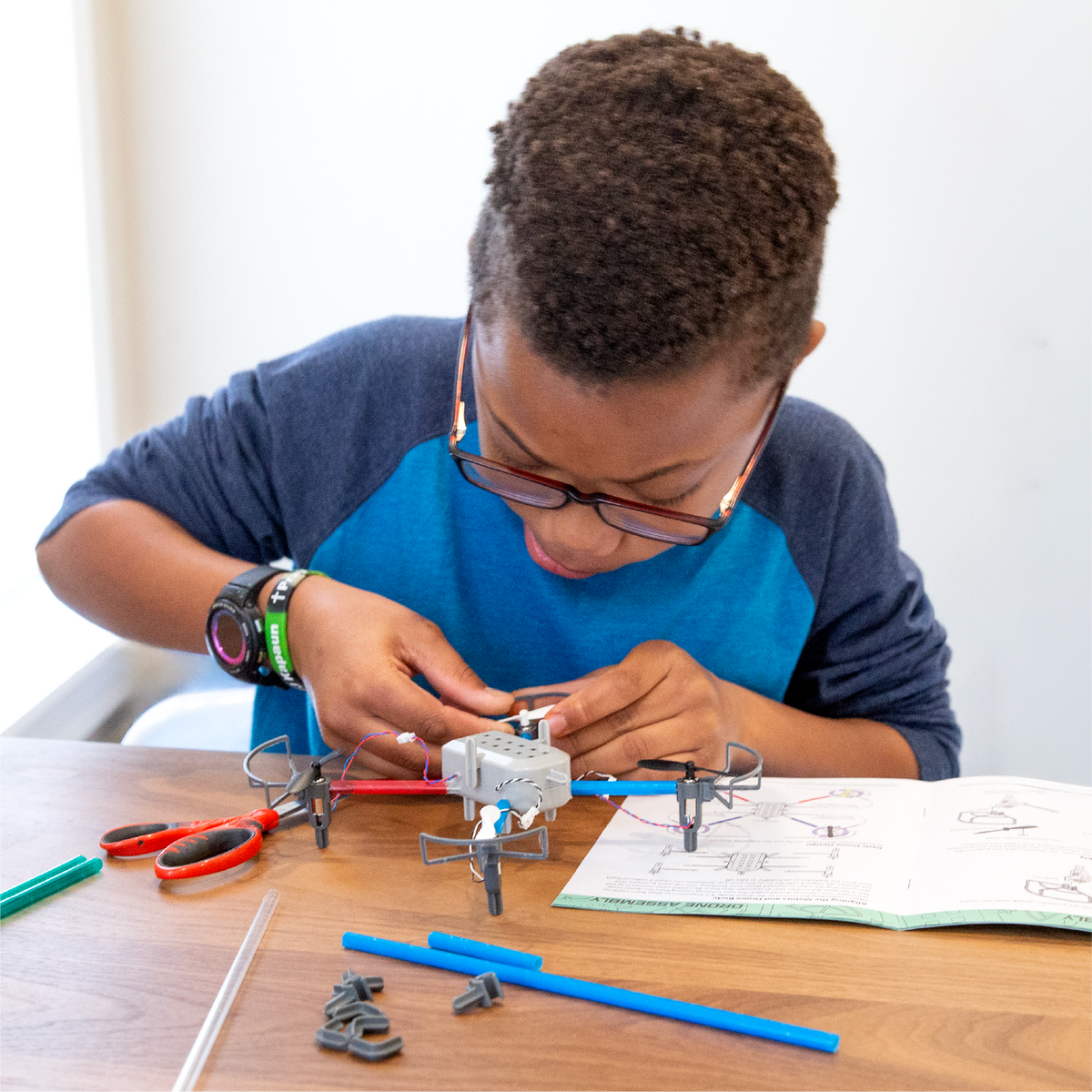 Child working on a drone maker kit at a table with tools and instructions.