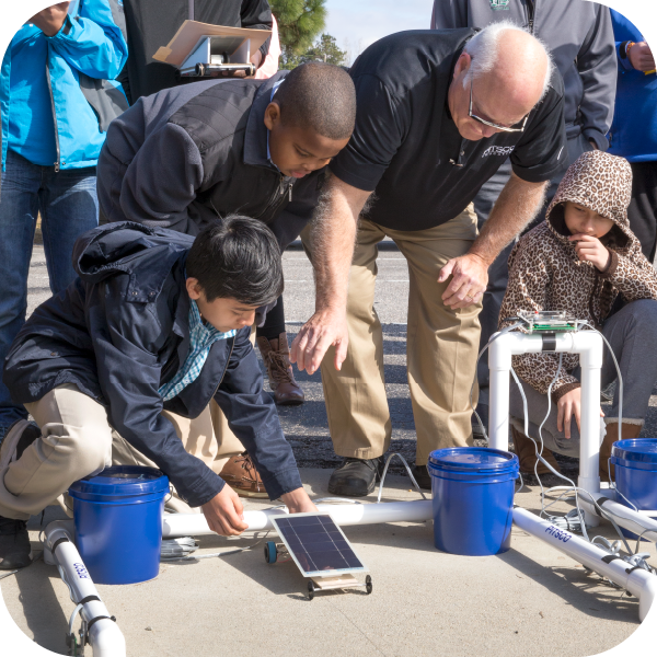 Group of students and a male teacher racing their Ray Catcher solar car outside