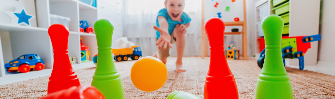 Child rolling a ball toward red and green toy bowling pins in a playroom