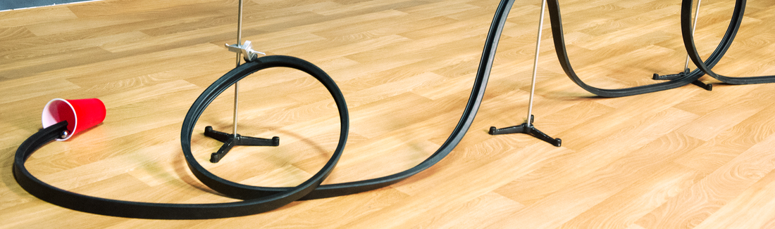Black flexible track looped over stands like a roller coaster with a red cup at the end on a wood floor