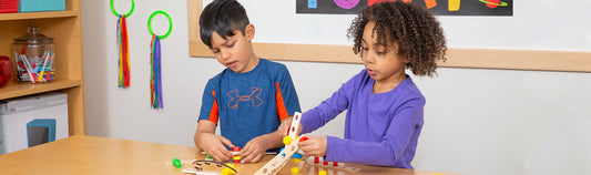 Two children building with wooden pegs and connector pieces at a classroom table
