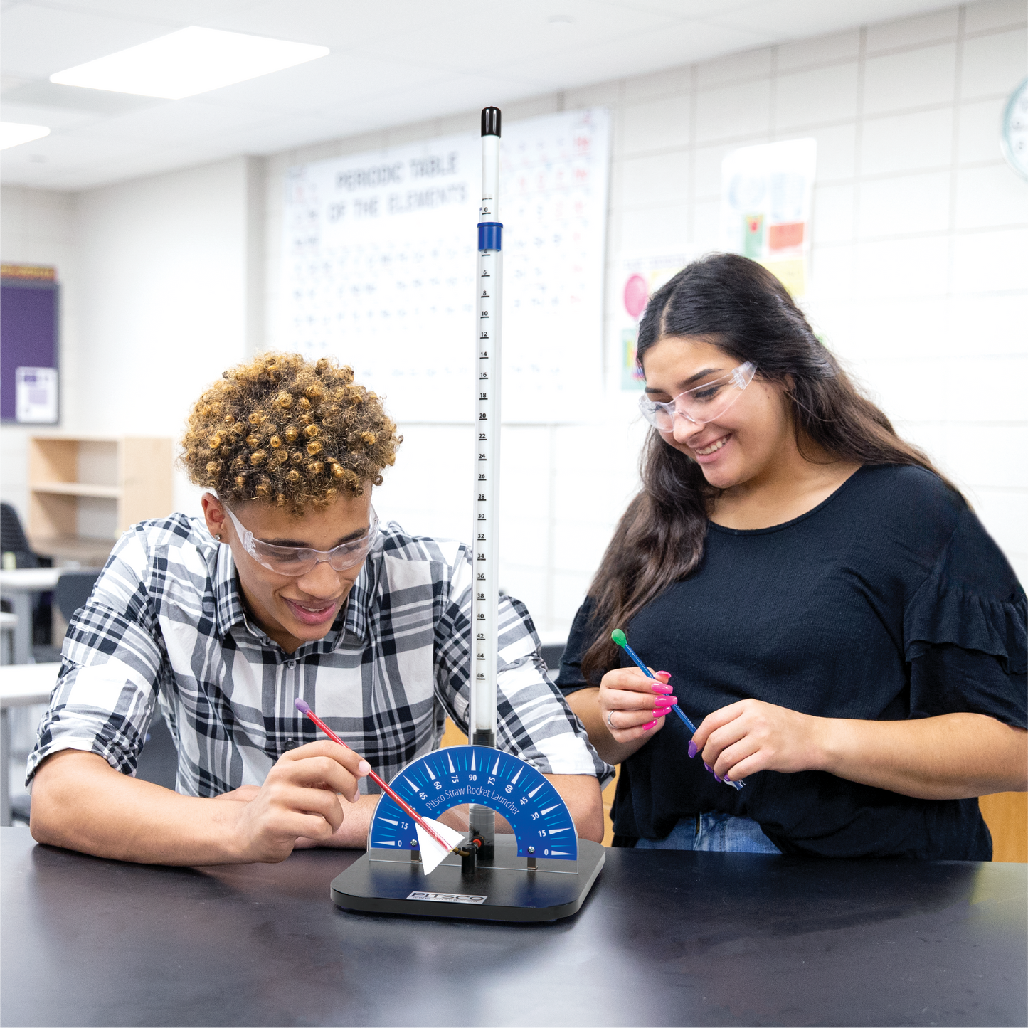 Two high school students in a classroom setting using a scientific instrument the Straw Rocket Launcher.