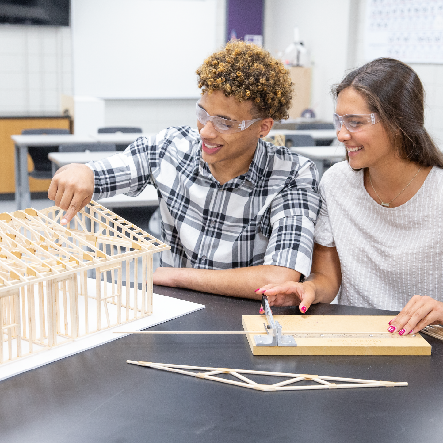 Two students in a classroom setting working on a construction project with wooden frames and tools.