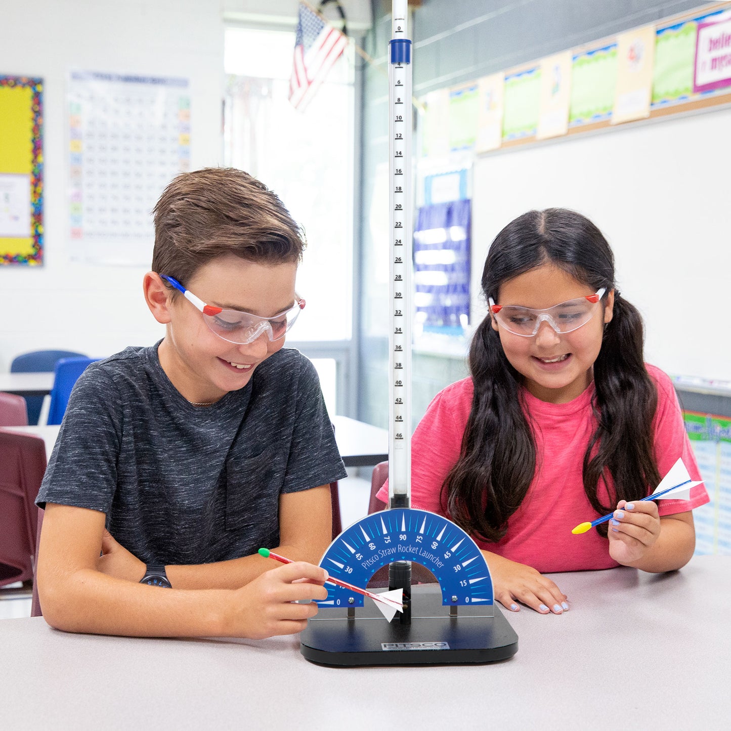 Girl and boy elementary aged students wearing safety glasses, using the straw rocket launcher in a classroom