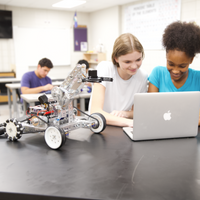 Two students working on a robot and using a laptop in a classroom setting.