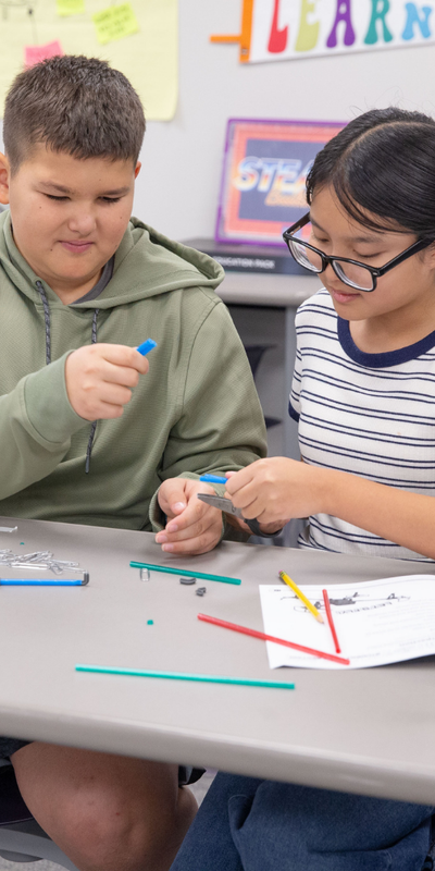 Two students building a drone with various materials