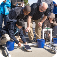 Group of students and a male teacher racing their Ray Catcher solar car outside