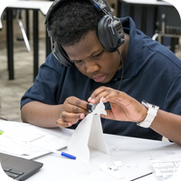 Male student wearing headphones assembling a wind generator in a classroom setting