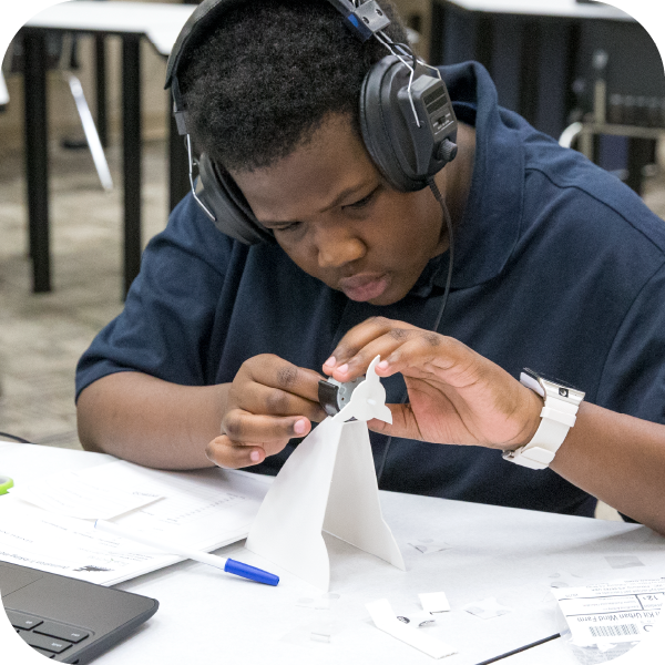 Male student wearing headphones assembling a wind generator in a classroom setting