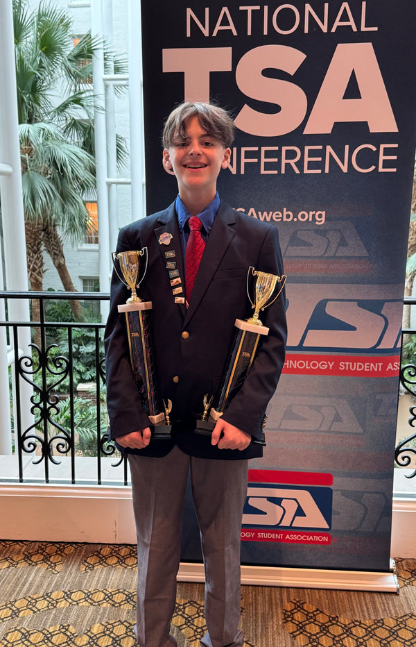 Boy holding two trophies in front of national TSA conference sign