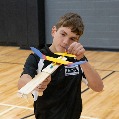 Student aiming a classroom glider during a hands-on aerospace STEM activity and engineering design challenge in a middle school physics classroom