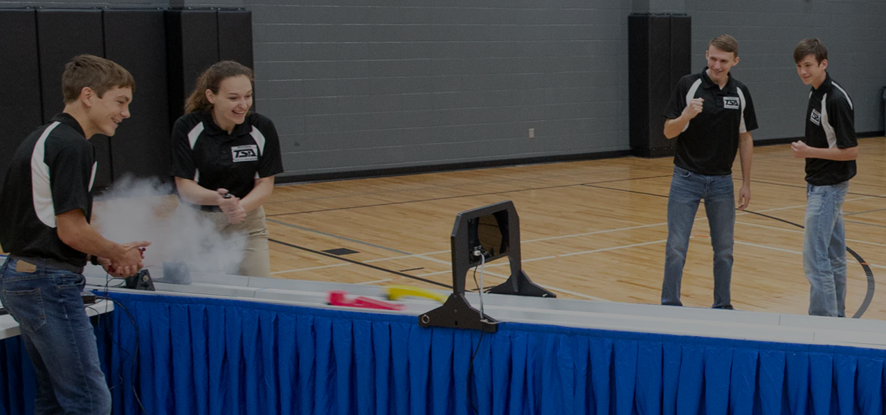 Four young people in a gym with two racing dragsters